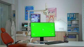Computer with green screen placed in front of camera in empty modern equipped stomatological room. Stomatology clinic with nobody in it prepared for next patient with mock-up, chroma key pc display video