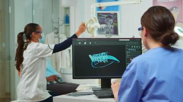 Dentist assistant writing parameters from digital dental fingerprint of patient, while specialist doctor with face mask speaks to man with toothache sitting on stomatological chair preparing tools video