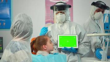 Stomatologist with coverall pointing at mockup greenscreen display during coronavirus epidemic. Explaining using monitor with green screen monitor chroma key izolated chroma pc key mock-up touchscreen video