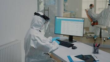 Stomatology nurse sitting at desk using modern computer, wearing ppe suit. Dental assistant looking at monitor typing on keyboard and orthodontist with oral care equipment examining patient video