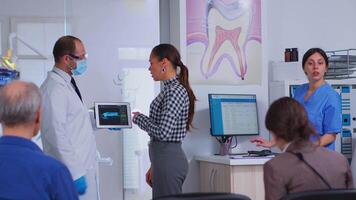 Doctor holding tablet with x-ray showing it to patient while nurse helping woman filling in dental document. Stomatologist presenting dental radiography using modern gadget in stomatological clinic video