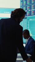 Vertical General director CEO sharing insight about a new development strategy with his employees, showing important data reports to analyze organizational activity status in a control room. Camera B. video