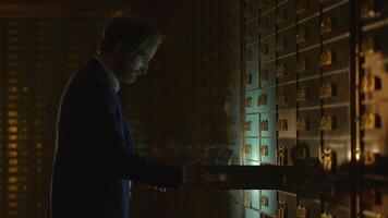 A man is carefully accessing safety deposit boxes in a dimly lit and shadowy vault video