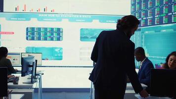 General director CEO sharing insight about a new development strategy with his employees, showing important data reports to analyze organizational activity status in a control room. Camera B. video