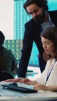 Vertical Enterprise colleagues reviewing project updates and details in monitoring room, establishing budget and other resources to achieve strategic business goals. Multiple corporation operations. camera A. video
