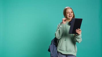 Radiant woman having funny conversation with friends during online teleconference using tablet, studio background. Upbeat girl having fun with mates during internet videocall on device, camera B video