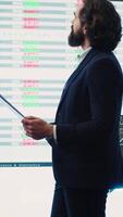 Vertical Chief executive officer reviews data shown on big display in the office, screens with infographics, finance analysis and organizational progress. Telecommunications system control room. Camera A. video
