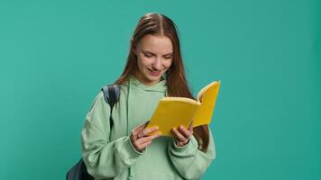 Young girl reading book, enjoying hobby, being entertained, isolated over studio background. Upbeat woman with novel in arms relaxing, having fun with interesting story, camera A video