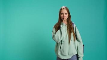 Stern woman doing shushing hand gesturing, irritated by noise, having negative mood. Girl placing finger on lips, doing quiet sign gesture, isolated over studio background, camera B video