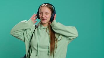 Happy girl wearing headphones having fun, dancing on rhythm, enjoying leisure time. Cheerful woman entertaining herself doing funky movements on music, studio background, camera A video