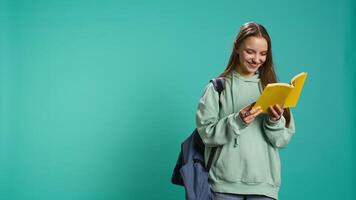 Young girl reading book, enjoying hobby, being entertained, isolated over studio background. Upbeat woman with novel in arms relaxing, having fun with interesting story, camera B video