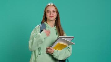 Portrait of smiling woman with backpack holding school notebook and notes, isolated over studio background. Cheerful girl with school supplies in arms, preparing to go to university, camera A video