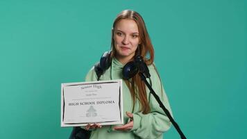 Happy student holding diploma talking in microphone, addressing audience, holding speech, studio background. Inspiring teenager using mic to share feeling during graduation ceremony, camera A video