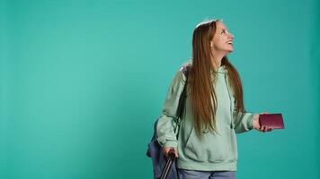 Joyous young traveler holding passport, going on vacation, looking around after arriving in new place. Happy girl travelling, sightseeing, visiting attractions, studio background, camera B video