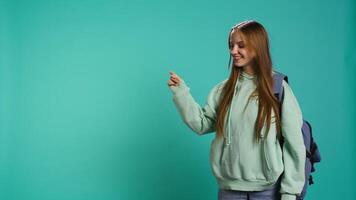 Radiant woman pointing finger towards empty space doing advertising, talking with audience. Smiling young girl doing presentation, showing copy text, studio backdrop, camera B video