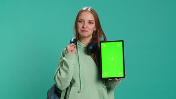 Portrait of woman presenting tablet with chroma key display, isolated over studio background. Young girl creating promotion with blank copy space mockup digital device, camera A video