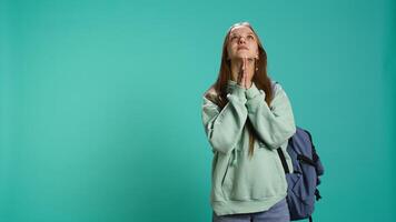 Hopeless young girl praying to deity for salvation. Religious teenager doing worship hand gesturing, asking for miracle, doing confession, isolated over studio background, camera B video