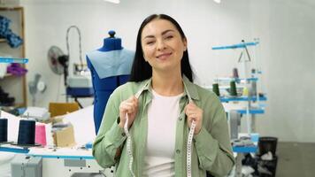 Portrait of a beautiful seamstress carrying a tape measure and working in a textile factory video