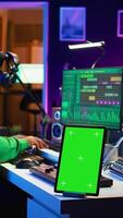 Vertical Composer editing his audio files and recordings on daw software, sitting next to a green screen display. Skilled sound technician uses mixing and mastering gear to produce new material. Camera B. video
