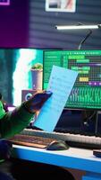 Vertical Artist pointing at musical sheet notation to explain notes on piano, teaching people to play synthesizer in home studio. Composer musician playing midi controller during online master class. Camera A. video