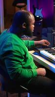 Vertical Sound engineer recording piano notes with DAW software in his home studio, working at night on producing new music with electronic tools. Musician composing tunes on midi controller. Camera B. video