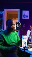 Vertical Artist pointing at musical sheet notation to explain notes on piano, teaching people to play synthesizer in home studio. Composer musician playing midi controller during online master class. Camera B. video