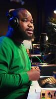 Vertical Confident artist singer performing a song on microphone in home studio, recording his audio files and manipulating raw sound on professional editing software. Music production. Camera B. video