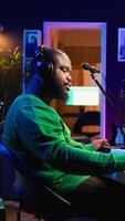 Vertical Professional artist writes new verses for a song in home studio, producing new music with mixing console and pc software. Composer works with audio equipment and tools, recording tunes. Camera B. video