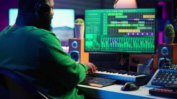 Audio engineer working in home studio with digital software on pc, playing piano keys and editing audio recordings. Musician producer creating tracks on midi controller keyboard notes. Camera A. video