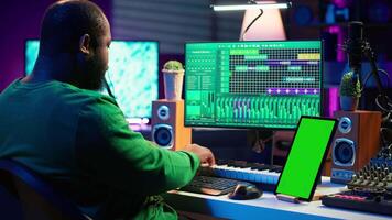 Songwriter composer mixing and mastering tracks next to green screen, operating on digital audio pc interface to add sound effects on new recordings. Technician in home studio. Camera A. video