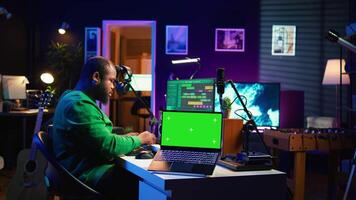 Producer editing his audio files and recordings on digital pc interface, sitting next to an isolated mockup screen. Sound engineer mixing and mastering songs with console in home studio. Camera B. video