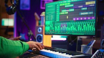African american audio technician using piano synthesizer keys to add sound effects in post production, editing tunes with digital software and mixing console. Male artist in home studio. Camera B. video