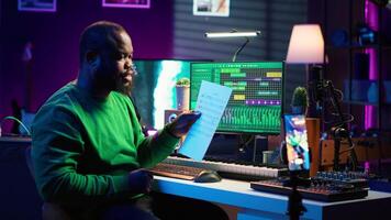 Artist pointing at musical sheet notation to explain notes on piano, teaching people to play synthesizer in home studio. Composer musician playing midi controller during online master class. Camera A. video