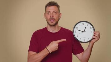 Handsome man showing time on wall office clock, ok, thumb up, approve, pointing finger at camera video