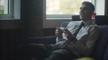 A business company's director takes a break from work in a modern office and indulges in gaming, using a joystick to play games on a TV, combining leisure and relaxation with a dash of office video