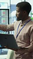 Vertical Business associates collaborating at the conference table in boardroom, utilizing smart technology and monthly statistics to present analysis of market trends and economic forecasts. Camera A. video