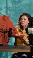 Vertical Upbeat content creator filming fashion vlog, showing audience jacket purchase she recently did. Joyous woman using professional equipment to record vlog, presenting viewers new clothes, camera A video
