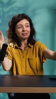 Vertical Smiling woman in studio using smartphone on selfie stick to record , greeting subscribers. Joyous entertainer hosts q and a session with viewers using cellphone, saluting fans, camera B video