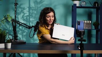 Internet show host using smartphone on phone holder, filming content about best gaming laptops. Media star recording notebook device review for interested viewers, camera B video