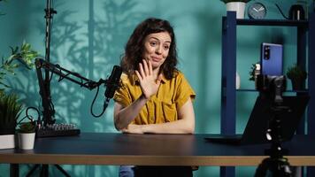 Influencer in home studio using smartphone on phone holder to record live broadcast, greeting subscribers. Internet star hosts q and a session with viewers using cellphone, camera B video