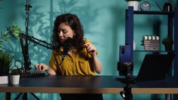 Content creator using smartphone to film ASMR for subscribers, tapping on mic. Woman in studio using professional microphone to whisper and put viewers to sleep, camera B video