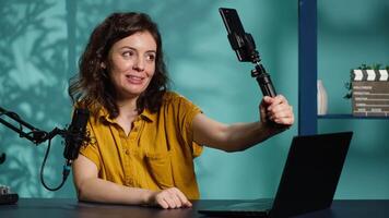 Influencer in home studio using smartphone on selfie stick to record live broadcast, greeting subscribers. Online star hosts q and a session with viewers using mobile phone, camera A video