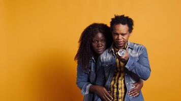 African american man using the flashlight to protect his scared terrified wife, afraid woman hiding behind her lover for protection against yellow background. Frightened moment. Camera B. video