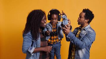 Enthusiastic father playing online games with baby boy using controller, both parents enjoying leisure time with their small kid. African american happy family play with joystick. Camera B. video