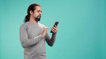 Portrait of smiling man talking with friends in phone call using smartphone, studio background. Jolly person feeling positive after receiving good news during telephone call, camera B video