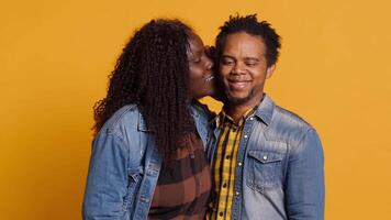 Affectionate romantic wife whispering intimate things to her husband, caressing and telling a secret into his ear. Cute optimistic couple flirting with each other, laughing in studio. Camera A. video
