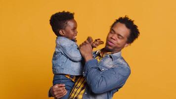 Playful smiling father embracing his cute infant toddler in studio, african american caring dad playing around with his little boy. Loving parent laughing and feeling happy with his son. Camera A. video