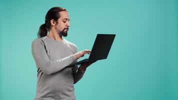 Portrait of smiling person spending time on laptop, isolated over studio background. Cheerful man checking social media posts on notebook, enjoying leisure time, camera B video