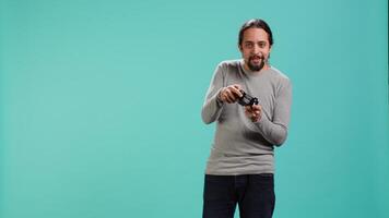 Cheerful player happy after winning gaming console game, shaking fist, studio background. Portrait of man satisfied after being victorious in videogame, defeating all enemies using gamepad, camera A video