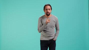 Portrait of man doing shushing hand gesturing, requesting silence. Person placing finger on lips, doing quiet sign gesture, asking for secrecy, isolated over studio background, camera A video